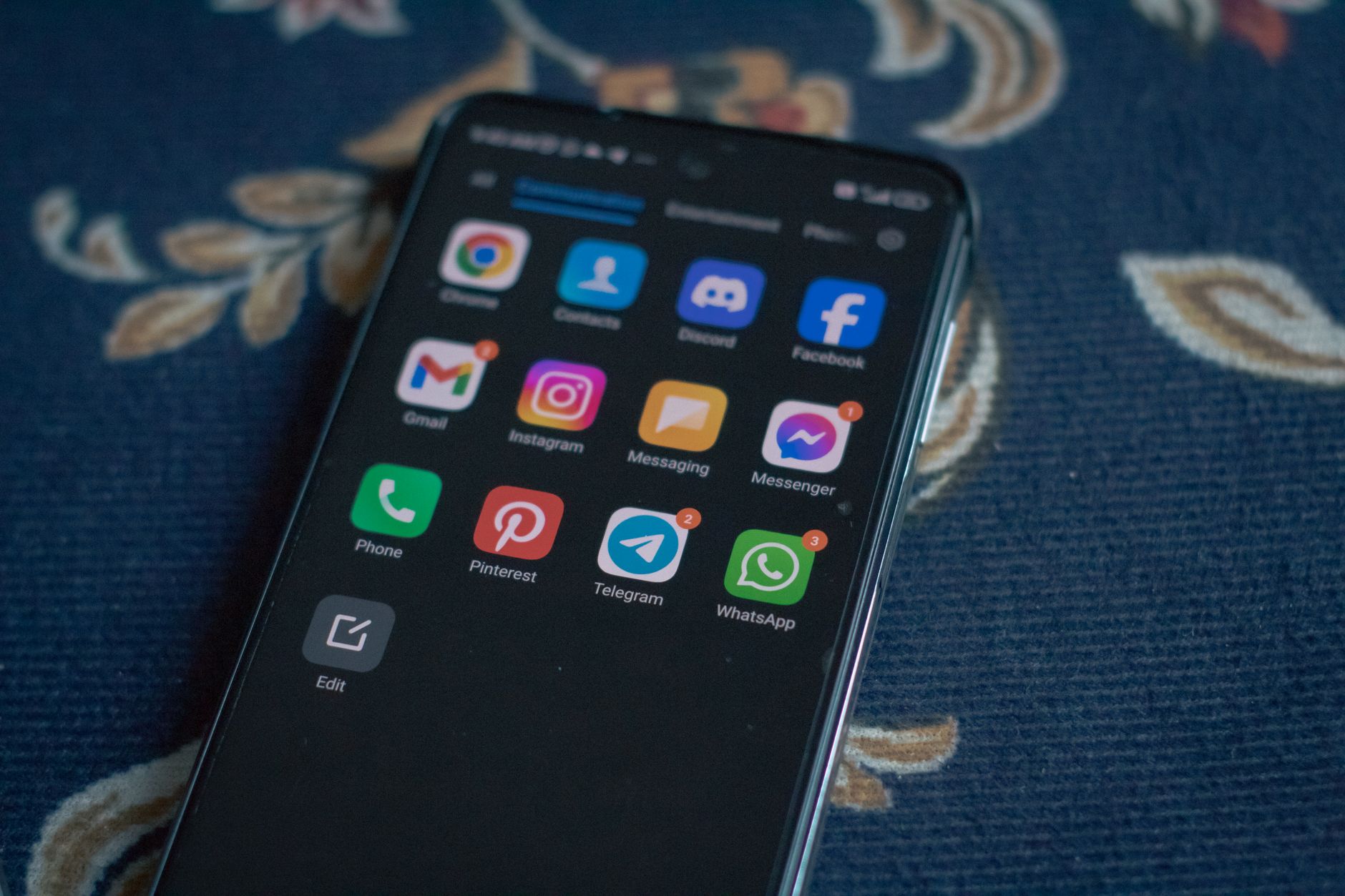 Close-up of a smartphone displaying popular social media apps on a floral fabric surface.